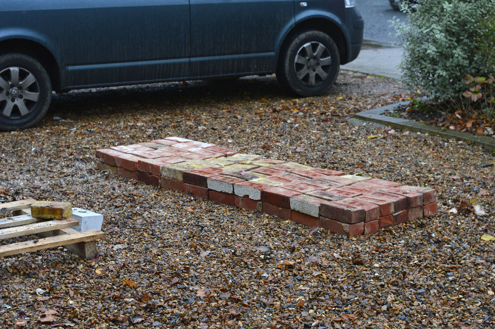 Bricks arranged in a two layer six-by-ten grid on a gravel floor